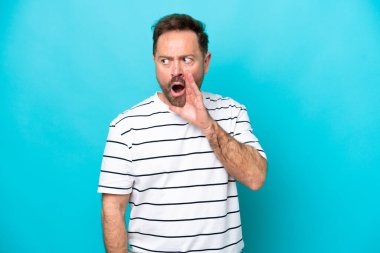 Mavi arka planda izole edilmiş orta yaşlı beyaz bir adam. Yan tarafa bakarken sürpriz bir jest yapıyor.