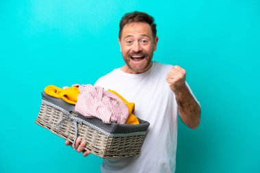 Mavi arka planda bir çamaşır sepetini tutan orta yaşlı kadın galibiyeti kutluyor.