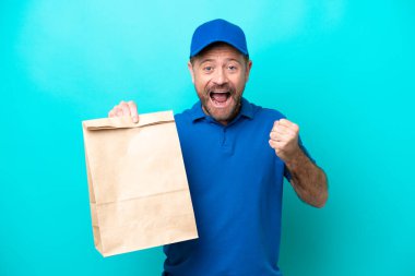 Orta yaşlı bir adam mavi arka planda izole edilmiş bir paket yiyecek alıyor ve galibiyeti kutluyor.