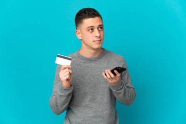 Kafkasyalı genç bir adam mavi arka planda izole edilmiş ve kredi kartıyla cep telefonu satın alıyor.
