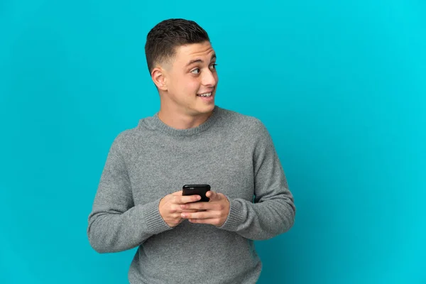 Joven Hombre Caucásico Aislado Sobre Fondo Azul Utilizando Teléfono Móvil — Foto de Stock