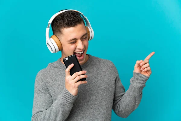 Joven Hombre Caucásico Aislado Sobre Fondo Azul Escuchando Música Con —  Fotos de Stock