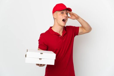 İş üniformalı bir pizzacı beyaz arka planda izole edilmiş pizza kutularını topluyor. Yan tarafa bakarken sürpriz jest yapıyor.