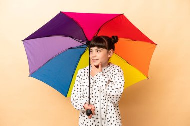 Bej arka planda izole edilmiş bir şemsiye tutan küçük kız yana bakıyor ve gülümsüyor.