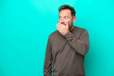 Mavi arka planda izole edilmiş orta yaşlı beyaz bir adam yan tarafa bakarken sürpriz jest yapıyor.