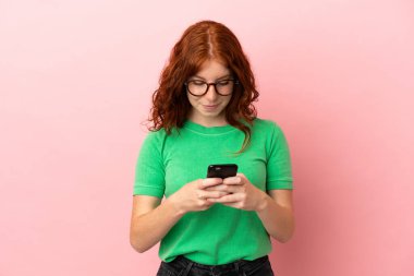 İzole edilmiş pembe geçmişi olan genç bir kızıl kız cep telefonuyla bir mesaj gönderiyor.