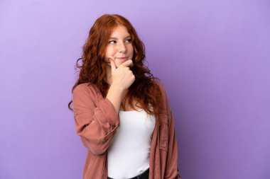 İzole edilmiş mor arka planda genç bir kızıl kız, yukarı bakarken bir fikir düşünüyor.