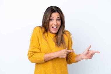 Beyaz arka planda izole edilmiş orta yaşlı beyaz kadın şaşırmış ve işaret ediyor.