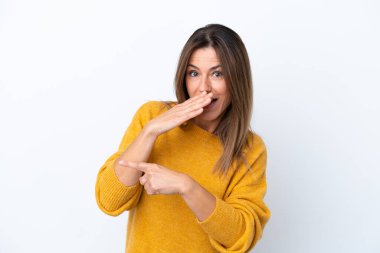 Beyaz arka planda izole edilmiş orta yaşlı beyaz kadın bir ürünü sunmak ve bir şeyler fısıldamak için kenarı işaret ediyor.