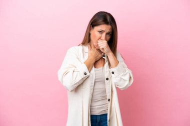 Orta yaşlı beyaz kadın, pembe arka planda izole edilmiş, çok öksürüyor.