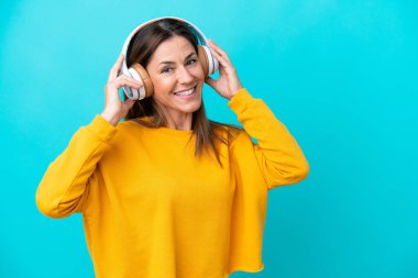 Orta yaşlı beyaz kadın mavi arka planda izole edilmiş müzik dinliyor.