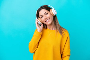 Orta yaşlı beyaz kadın mavi arka planda izole edilmiş müzik dinliyor.