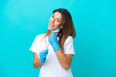 Mavi arka planda izole edilmiş orta yaşlı doktor kadın zaferi kutluyor.