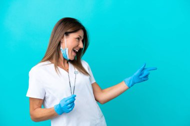 Mavi arka planda izole edilmiş orta yaşlı doktor kadın parmağını yana uzattı ve bir ürün sundu.