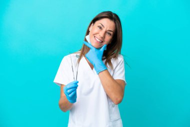 Mavi arka planda izole edilmiş orta yaşlı doktor kadın mutlu ve gülümsüyor.