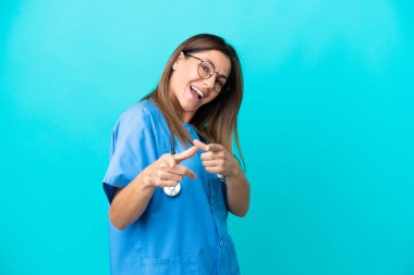 Mavi arka planda izole edilmiş orta yaşlı cerrah kadın ön tarafı gösteriyor ve gülümsüyor.