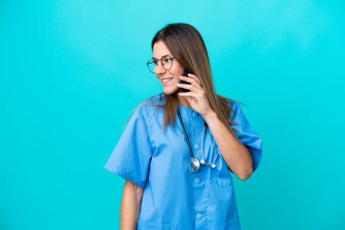 Mavi arka planda izole edilmiş orta yaşlı cerrah kadın cep telefonuyla biriyle sohbet ediyor.