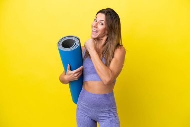 Spor kadını yoga derslerine giderken elinde sarı olmayan bir minder tutarak zaferi kutluyor.