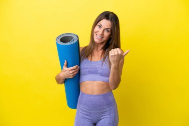 Elinde paspas tutarken yoga derslerine giden sporcu kadın sarı olmayan bir arka planda el ele davet ediyor. Gelmene sevindim.