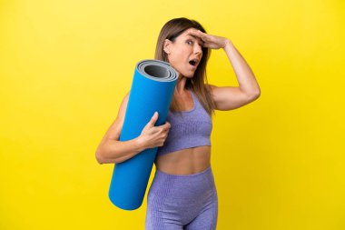 Spor kadını yoga derslerine giderken elinde bir paspas tutarken sarı olmayan bir arkaplan yan tarafa bakarken sürpriz jest yapıyor.