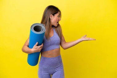 Elinde paspas tutarken yoga derslerine giden sporcu kadın sürpriz bir ifadeyle sarı olmayan bir zemin tutuyor.