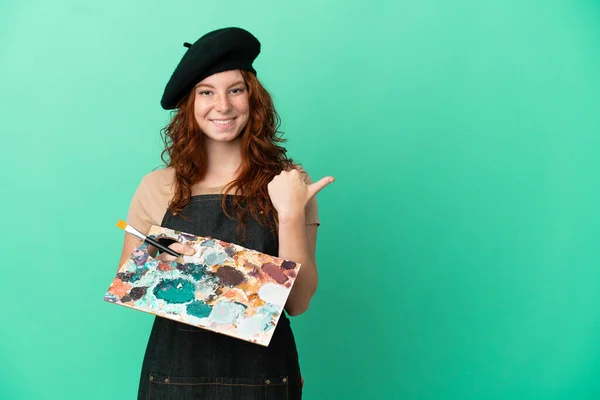 Nastoletni Rudowłosy Artysta Trzymający Paletę Odizolowanych Zielonym Tle Wskazując Bok — Zdjęcie stockowe