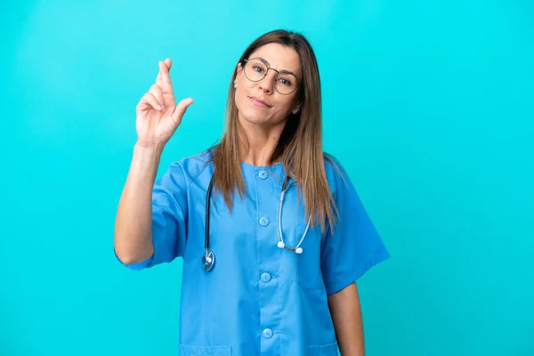 中年妇女外科医生 以蓝色背景隔离 手指交叉 并祝愿她最好 — 图库照片