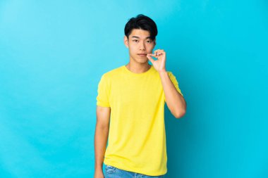 Mavi arka planda izole edilmiş genç bir Çinli sessizlik işareti gösteriyor.