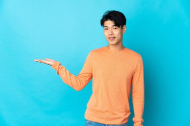 Mavi arka planda izole edilmiş genç bir Çinli davet etmek için ellerini yana uzatıyor.