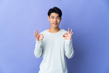 Mor arka planda izole edilmiş genç bir Çinli iki eliyle tamam işareti gösteriyor.