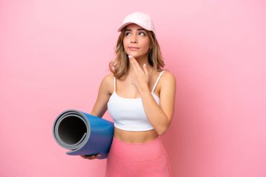 Genç sporcu kadın yoga derslerine giderken elinde minderle yukarı bakıp gülümsüyor.