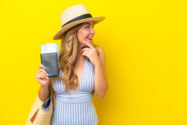 Genç bir kadın, sarı arka planda izole bir şekilde tatile çıkar. Bir fikir üretir ve bir tarafa bakar.