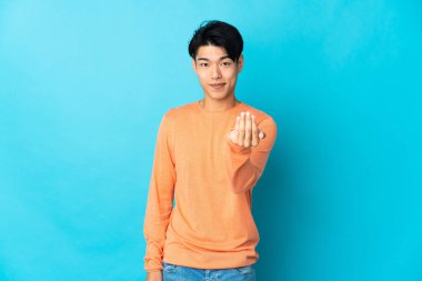 Genç Çinli bir adam mavi arka planda izole edilmiş ve davet edilmişti. Gelmene sevindim.