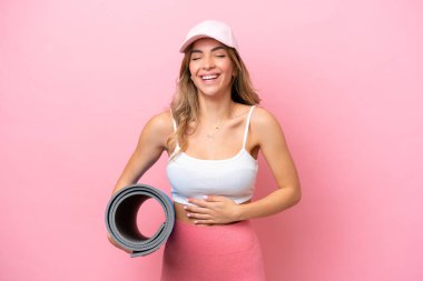 Genç sporcu kadın yoga derslerine giderken elinde minderle gülümsüyor.