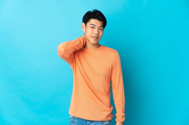Genç Çinli adam mavi arka planda yalnız gülüyor.