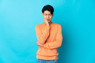 Mavi arka planda diş ağrısı olan genç bir Çinli izole edilmiş.