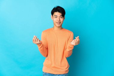 Genç Çinli adam mavi arka planda izole edilmiş para hareketi yapıyor.