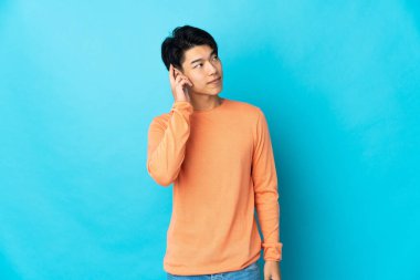 Genç Çinli bir adam mavi arka planda izole edilmiş bir fikir düşünüyor.