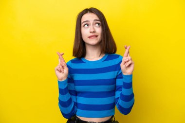Sarı arka planda izole edilmiş genç Ukraynalı kadın parmaklarını çapraz yapıp en iyisini diliyor.