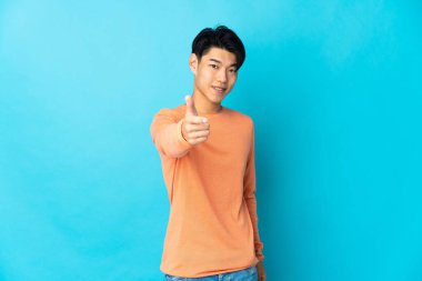 Genç Çinli adam mavi arka planda izole edildi. Başparmakları havada çünkü iyi bir şey oldu.