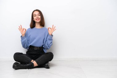 Genç Ukraynalı kadın, beyaz arka planda izole bir şekilde yerde oturuyor. Parmaklarıyla 