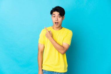 Young Chinese man isolated on blue background surprised and pointing side