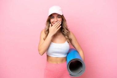 Genç sporcu kadın yoga derslerine giderken elinde minderle mutlu ve gülümseyen bir ağızla el ele tutuşuyor.