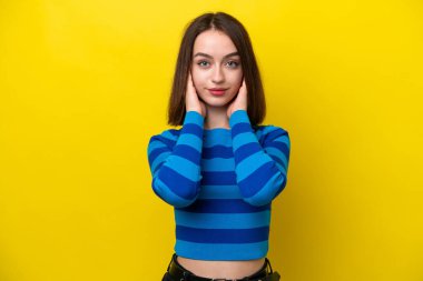 Sarı arka planda izole edilmiş genç Ukraynalı kadın hayal kırıklığına uğramış ve kulaklarını kapatmış.