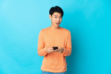 Mavi arka planda izole edilmiş genç bir Çinli şaşırmış ve bir mesaj göndermiş.