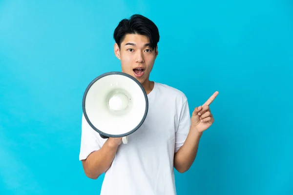 Young Chinese Man Isolated Blue Background Shouting Megaphone Pointing Side — Stockfoto