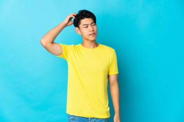 Genç Çinli bir adam mavi arka planda izole edildi. Kafasını kaşırken şüpheleri vardı.