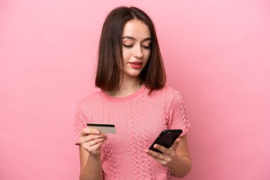 Pembe arka planda izole edilmiş genç Ukraynalı bir kadın kredi kartıyla cep telefonuyla alışveriş yapıyor.