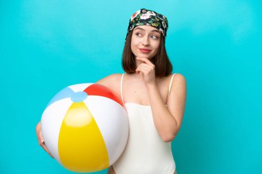Young Ukrainian woman holding beach ball isolated on blue background and looking up