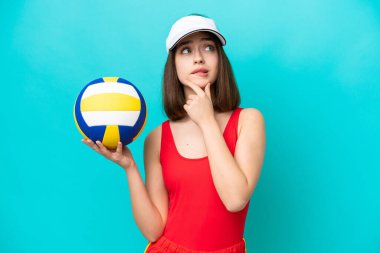 Genç Ukraynalı bir kadın plajda voleybol oynuyor. Mavi arka planda izole edilmiş. Şüpheleri ve düşünceleri var.